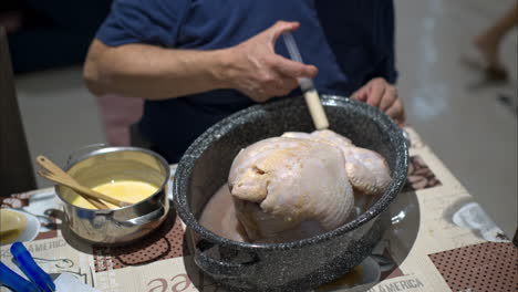 close up of the hands of an hispanic mature man injecting a concoction of his own to a raw turkey preparing for christmas thanksgiving