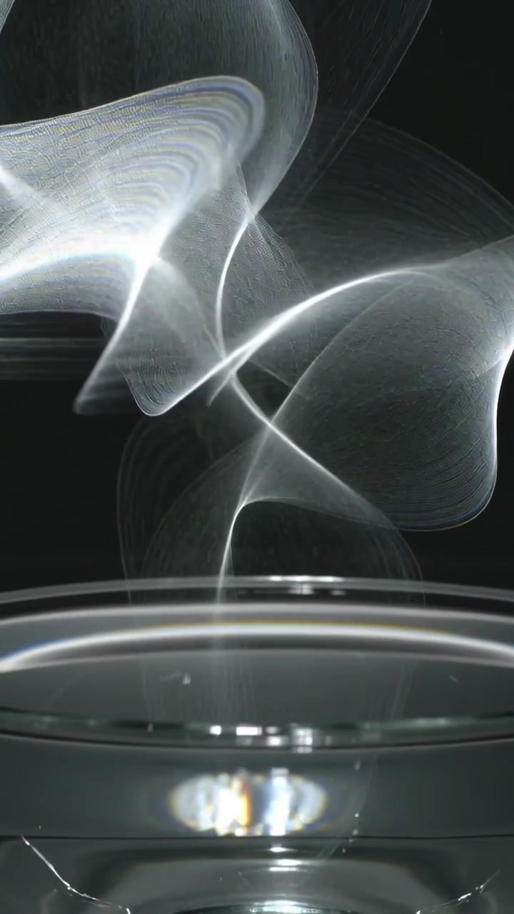 Vertical video: Falling thin ribbon causing twisting over glass bowl on table, making center glow