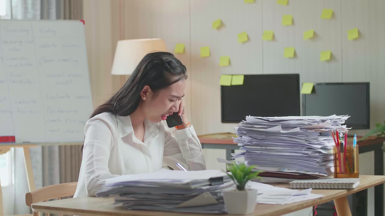 Asian Woman Talking On Phone And Taking Note While Working Hard With Documents At Office