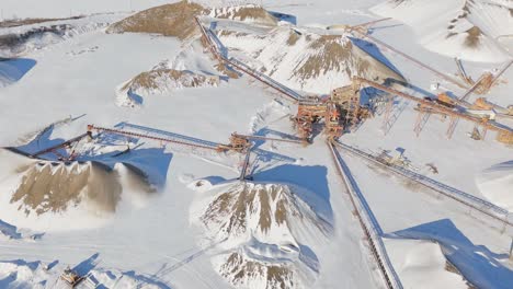 wide forward aerial of stone crusher machine at quarry in snowy canada