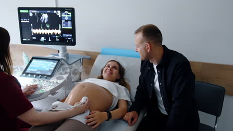 caucasian couple having pregnancy examination at modern clinics. happy parents smile to each other.