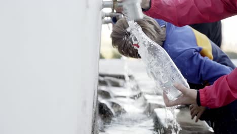 persona llenando una botella de vidrio de agua, y un niño bebiendo agua de un grifo natural