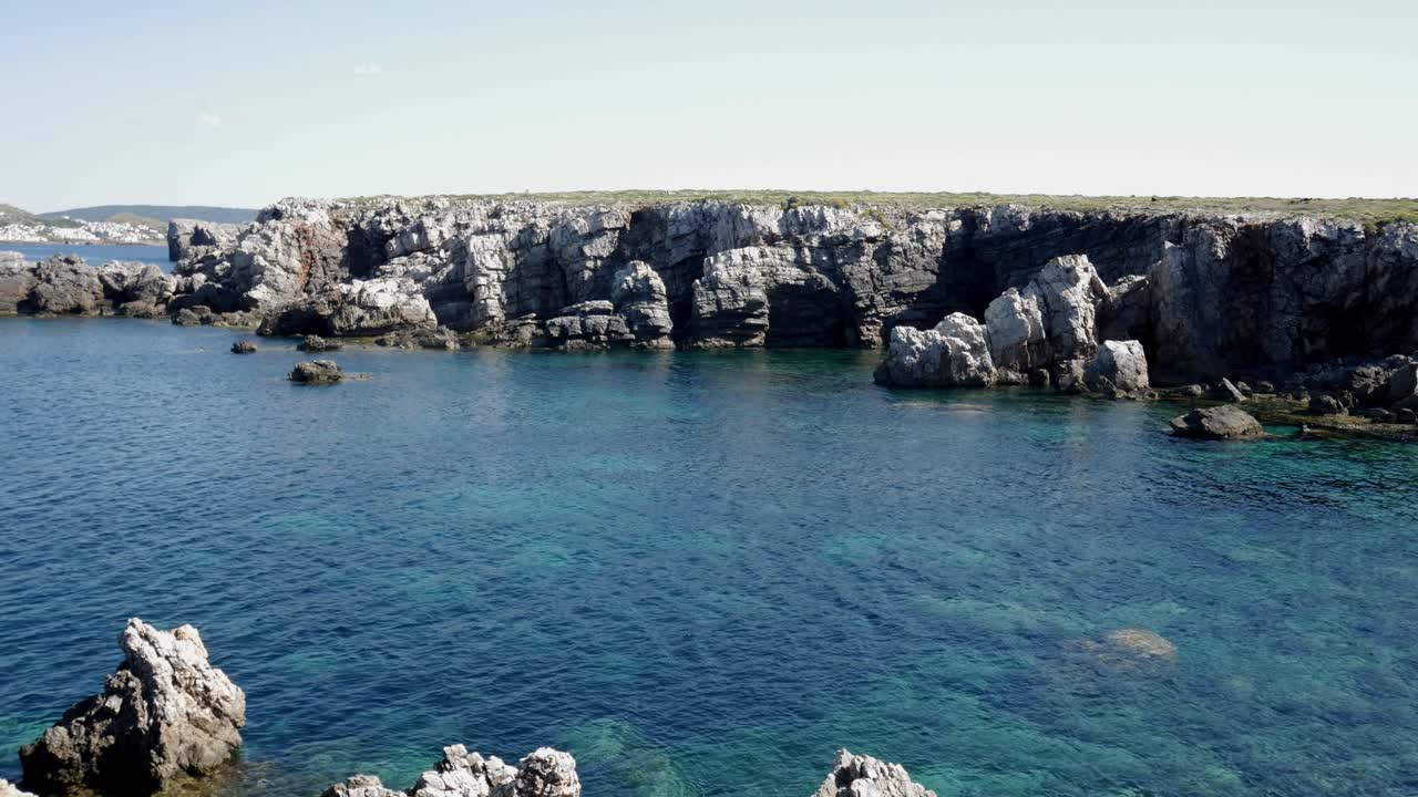 Crystal-clear blue waters meet rugged limestone cliffs in Cala Viola De Levant, Menorca