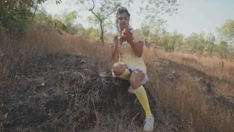 an attractive asian female carefully painting a clay pot sitting on a rock in a dry grass field on a beautiful day outdoors in nature, india