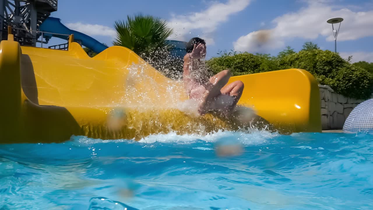 descenso del tobogán acuático en un parque acuático de vacaciones. cámara lenta en un tobogán acuático vacaciones familiares, una mujer en bikini desciende del tobogán en una piscina de agua azul salpicando gotas de agua.