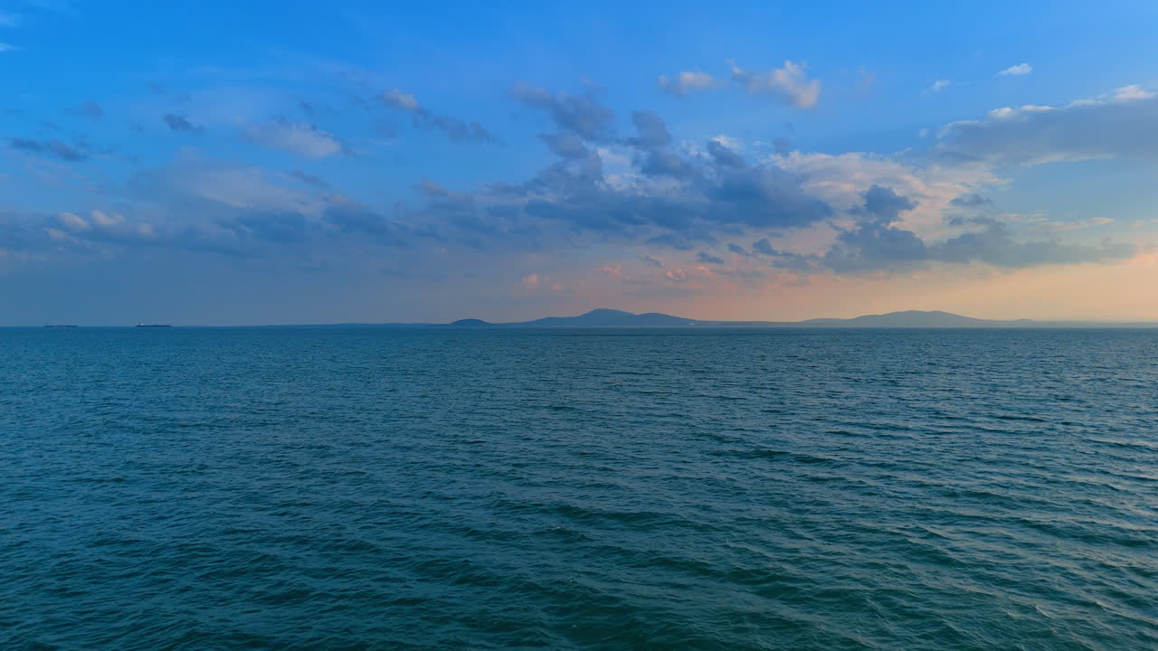 Ampio paesaggio marino con uccello in volo e montagne distanti sotto un cielo blu. Vista orizzontale di acqua di mare calma con un singolo uccello e la silhouette di una montagna all'orizzonte.