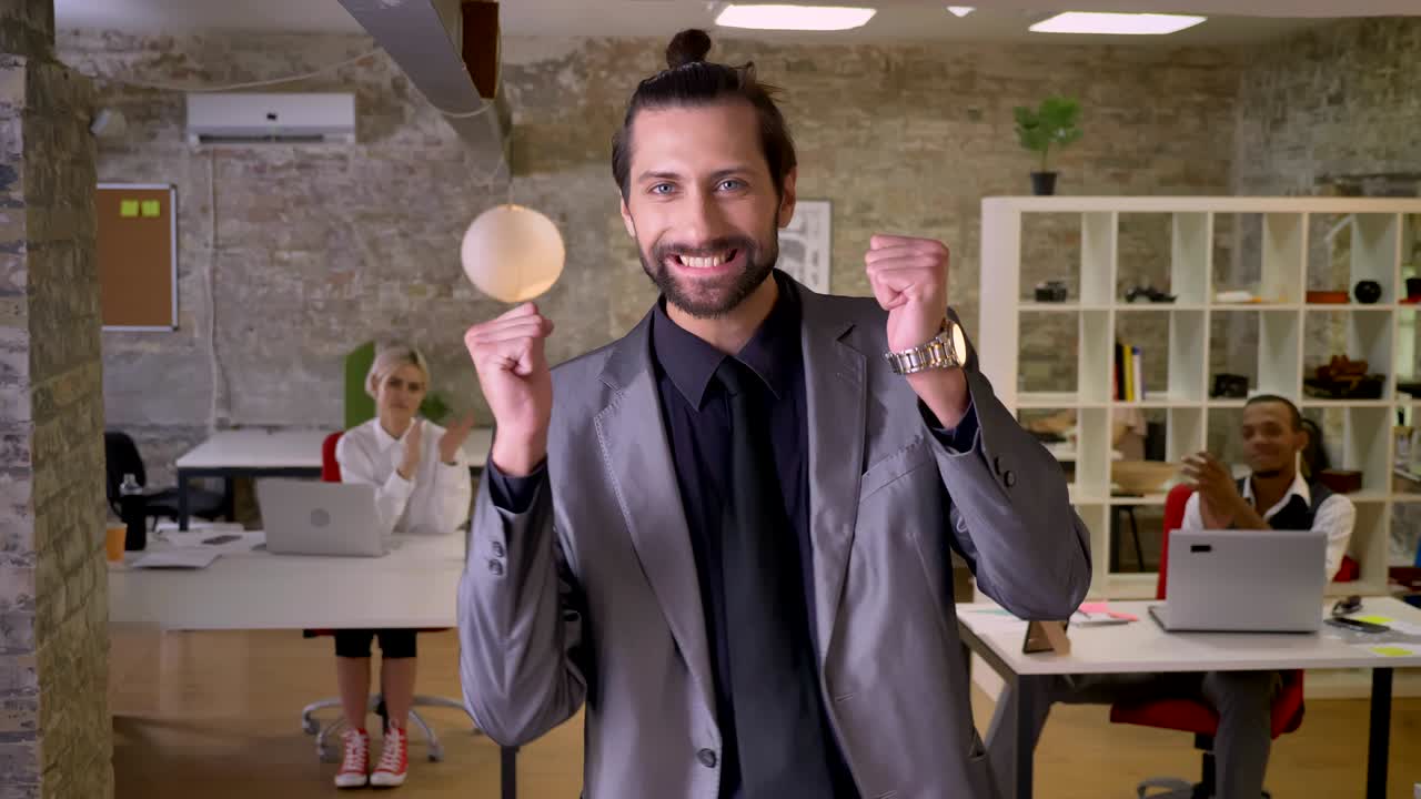 un hombre de negocios alegre con barba está bailando en la oficina, sonriendo, los colegas están aplaudiendo, concepto de trabajo, concepto de relajación