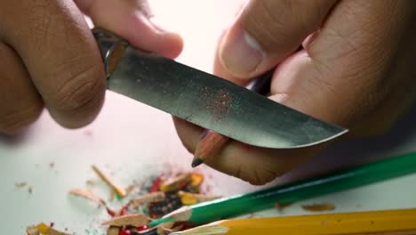 imágenes de manos afilando lentamente un lápiz y algunos lápices de colores con un cuchillo afilado