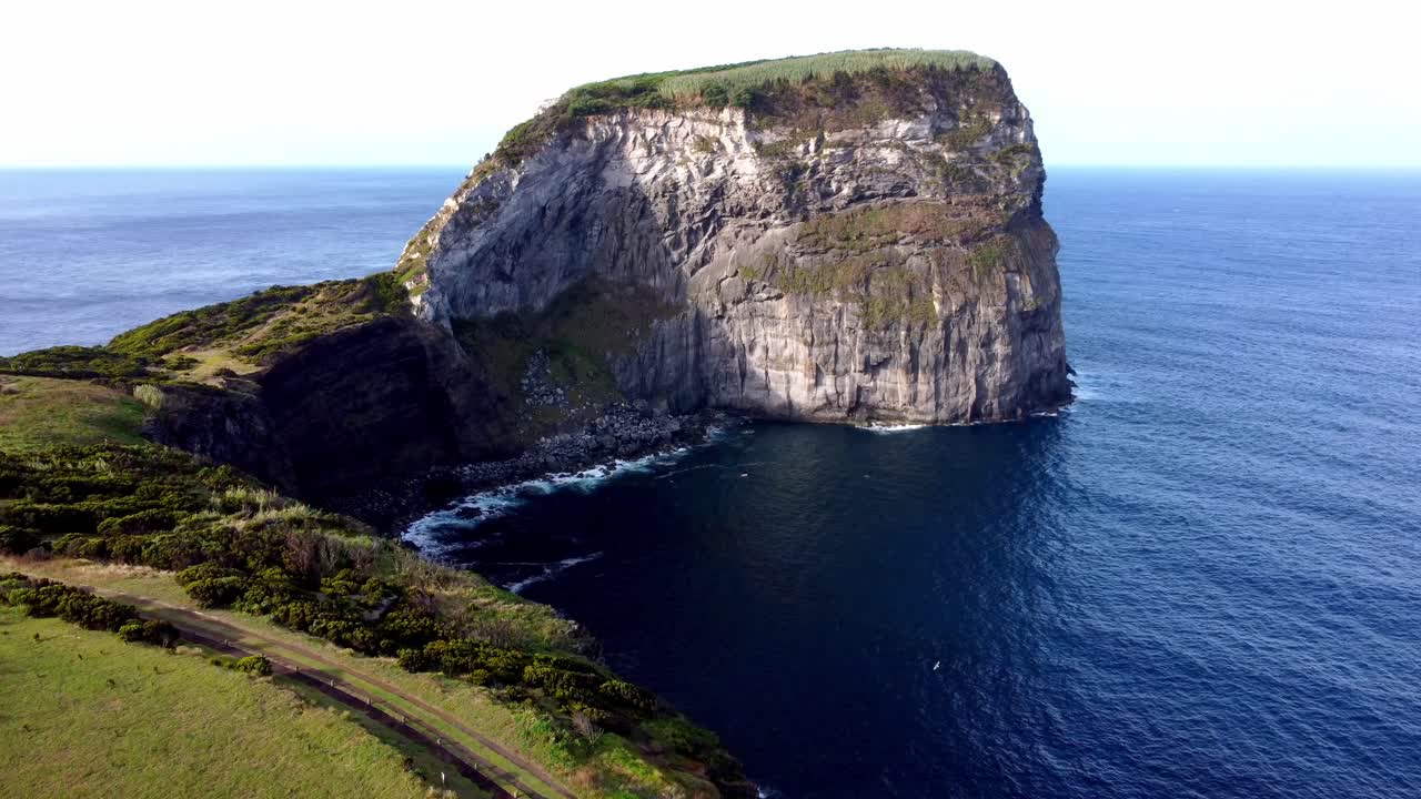 Sweeping aerial view over the Morro de Castelo Branco headland on Faial Island, surrounded by blue Atlantic waters