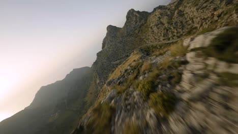 fpv drone shot flying low over sa calobra road along rocky mountain range in mallorca, spain during evening time