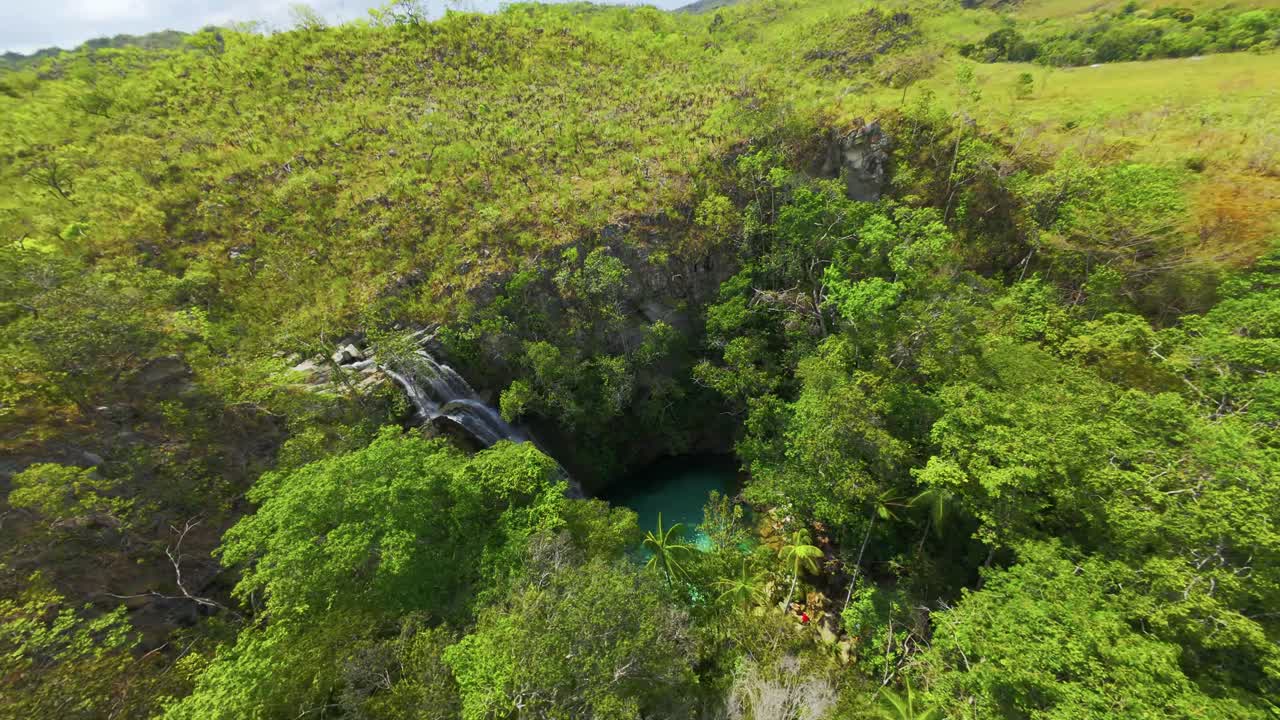 Cascading Santa Bárbara waterfall flows into a stunning turquoise pool, surrounded by lush vegetation in Chapada dos Veadeiros National Park, Goiás, Brazil, orbiting fpv pov drone shot