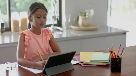 focused biracial girl having elementary school class on tablet in kitchen, copy space, slow motion