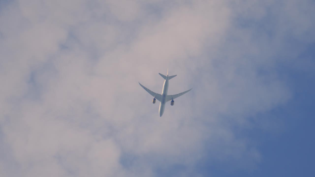 Commercial Airliner Flying Overhead with Wings and Engine Detail Against White Clouds. Passenger Aircraft Carrying People Around the World