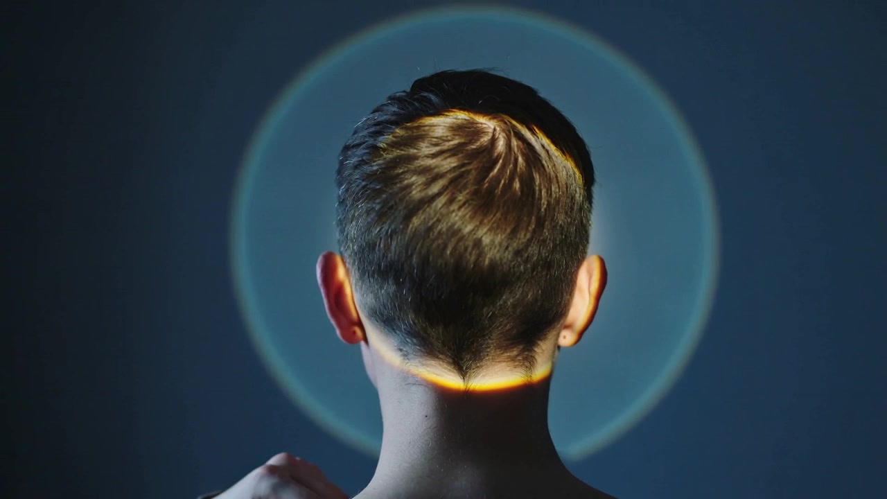Persona con maglia a maniche lunghe che sistema la scollatura, con un'aureola che appare, abbassando la mano in studio, con una fascia arancione al collo.