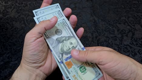 Close-up-of-hands-counting-US-banknotes-on-a-table-with-a-dark-background