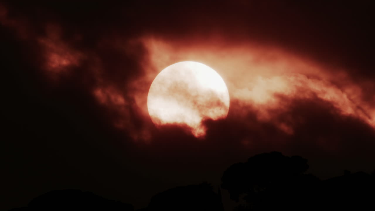 A glowing red sun partially covered by dark clouds at dusk