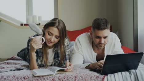 couple relaxing on bed with laptop and book