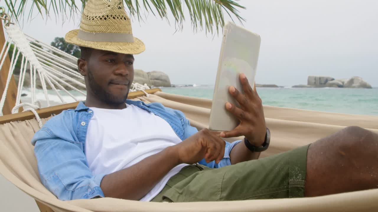 Front view of African american man using digital tablet on the beach 4k