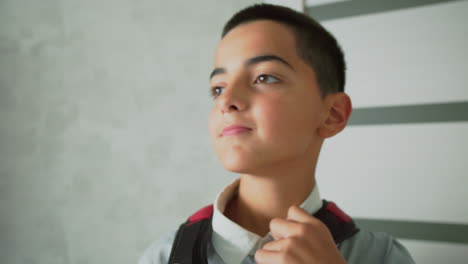 boy confidently putting backpack on shoulder while preparing for school in bright home hallway, dressed in light shirt, showing readiness and positive attitude in peaceful domestic morning setting