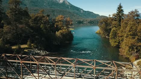 el dron se eleva desde el agua hasta la cima de un viejo puente de metal para ver el paisaje otoñal con el lago al fondo.