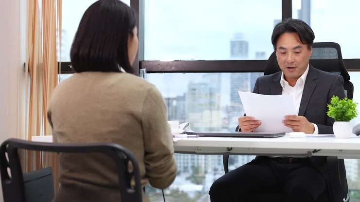 Professional male recruiter reviews documents while talking to a candidate in a bright office