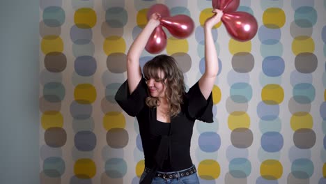 Young-Woman-Dancing-and-Holding-Balloons-in-Hand-Against-Colorful-Background