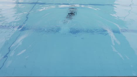 Vista-Posterior-De-Un-Joven-Con-Gorra-Y-Gafas-Deslizándose-Y-Buceando-En-La-Piscina.