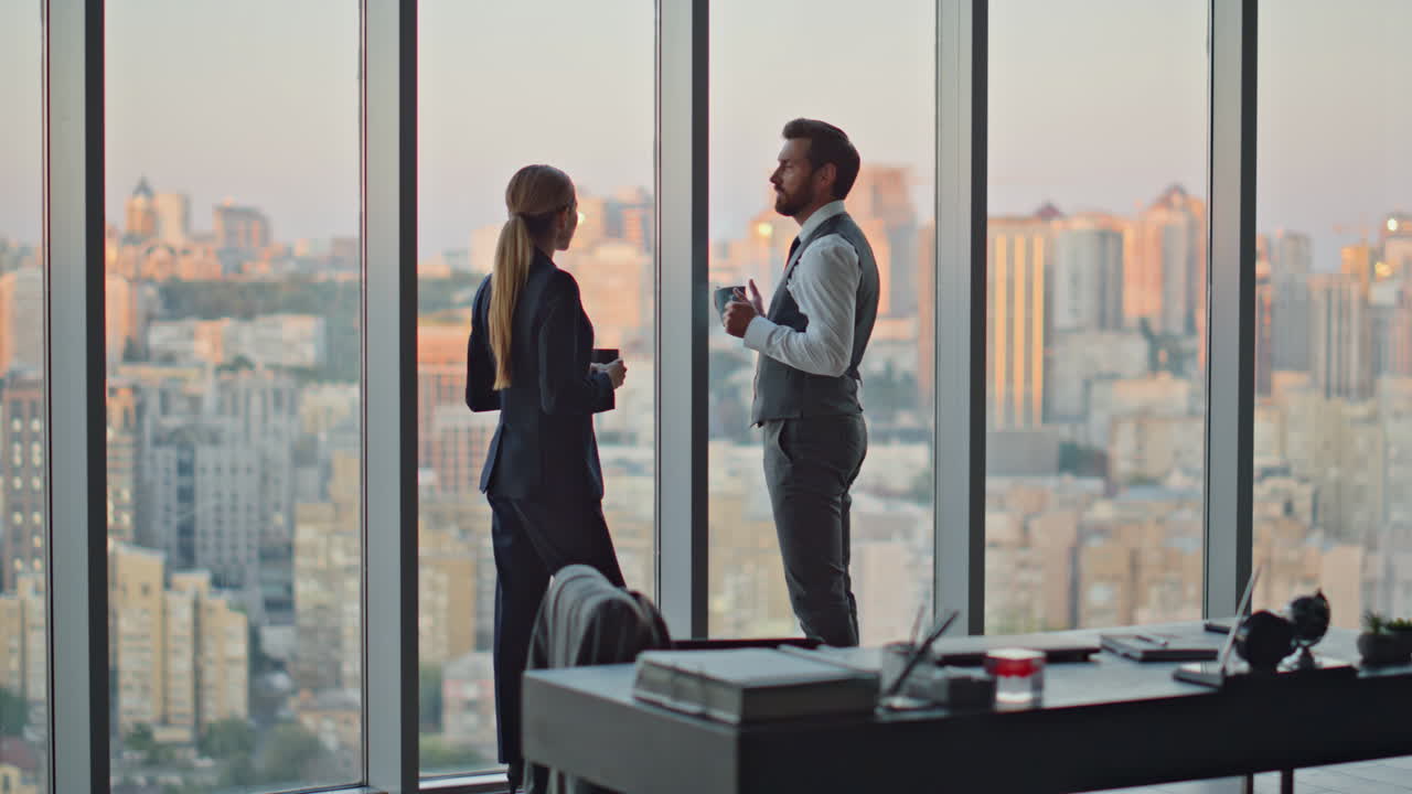 Geschäftspaar unterhält sich am Abend mit Blick auf die Stadt. Firmenmitarbeiter entspannen sich im Büro.
