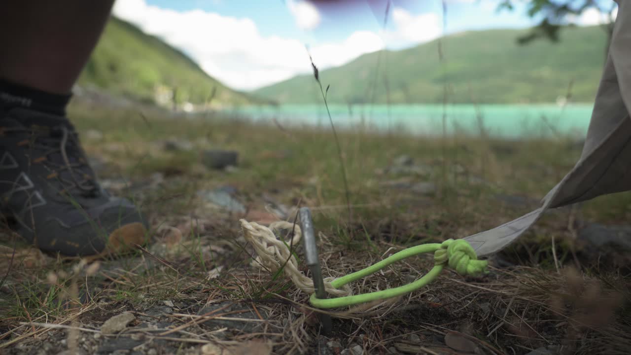 Camper Hammering Tent Stake On The Ground Using A Rock. - close-up shot