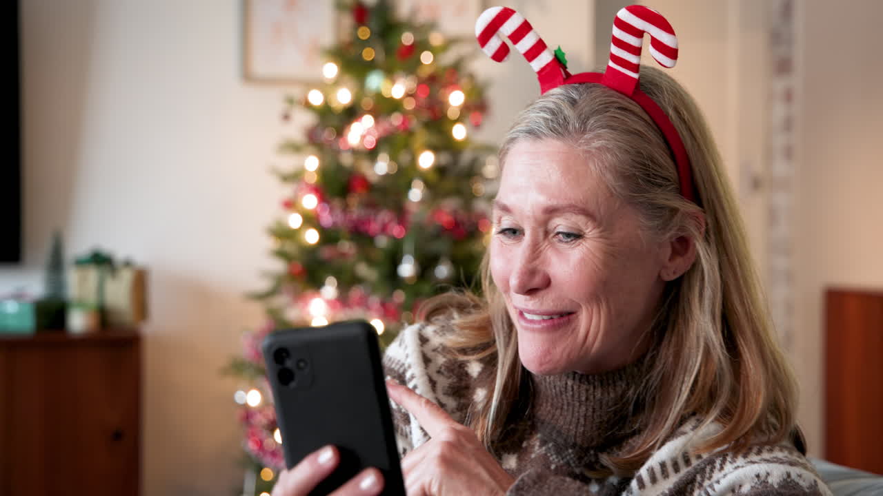 Smiling woman with smartphone enjoying Christmas near decorated tree at home