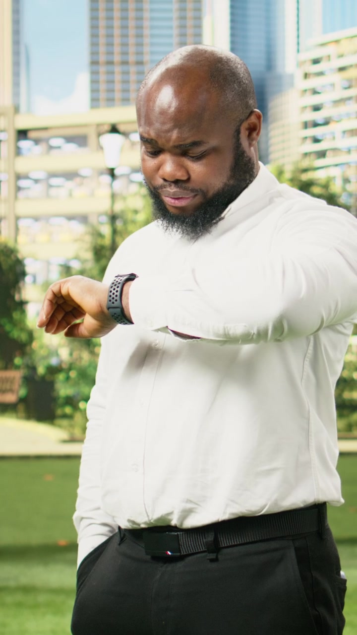 Vertical Video Worried businessman looking down at smartwatch while standing outdoors