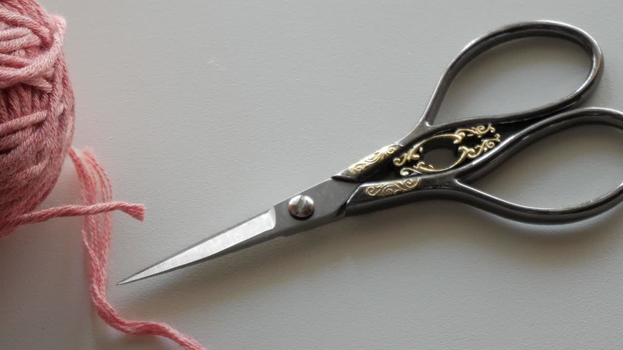 slight camera movement over a pastel coloured wool - threads of the wool and a shear lie on the table