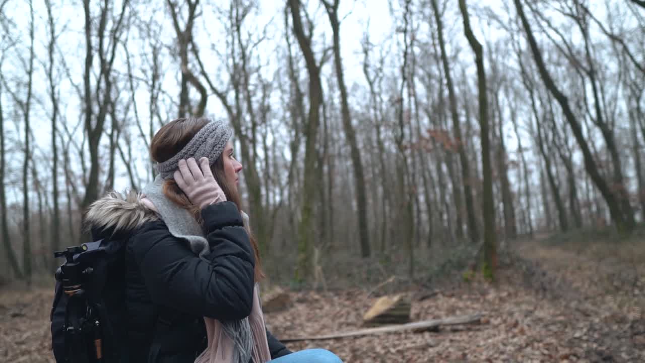 Young female caucasian photographer sitting on stump and touching her gray headband with her hand wearing pink glove