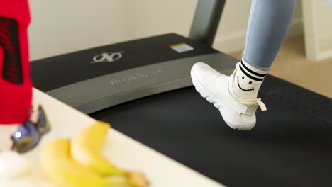person jogging on treadmill with focus on feet, surrounded by fitness gear and bright lighting
