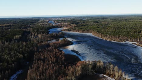 Stunning aerial view of a beautiful frozen lake in a vast forest in rural forest on a sunny winter day in Sweden