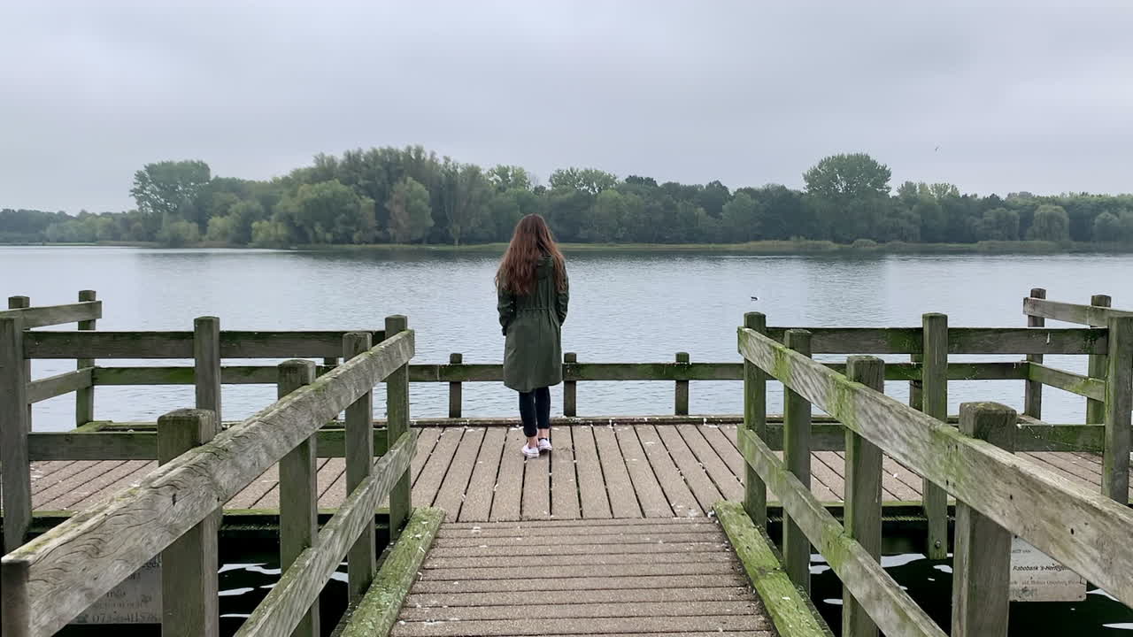 Slow motion shot of a young, elegant girl walking down on a dock at the lakeside, at November.