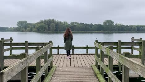 slow motion shot of a young, elegant girl walking down on a dock at the lakeside, at november.