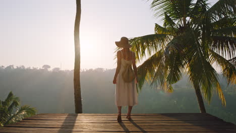 travel woman with arms raised celebrating vacation with arms raised enjoying beautiful view of tropical jungle from deck at sunrise 4k