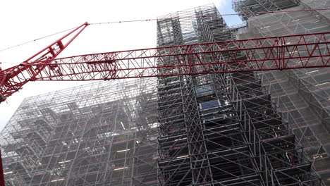 Construction-Crane-and-Scaffold-Attached-to-Building,-Low-Angle-Pan