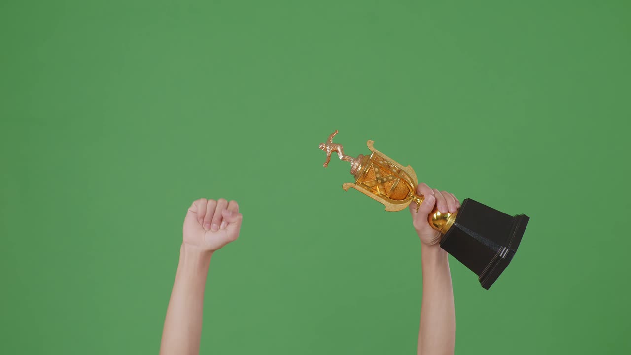 한 남자의 손이 트로피를 들고 있다. 녹색 화면 배경