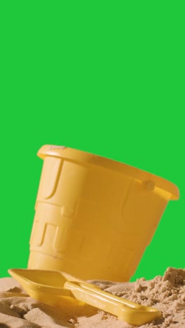 Vertical-Video-Summer-Holiday-Concept-With-Child's-Bucket-Spade-On-Sandy-Beach-Against-Green-Screen