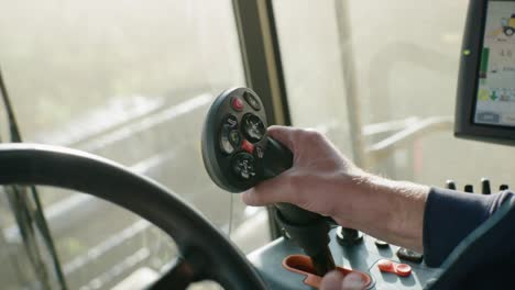 hand controlling joystick inside combine harvester cabin harvesting organic soybeans on sunny day