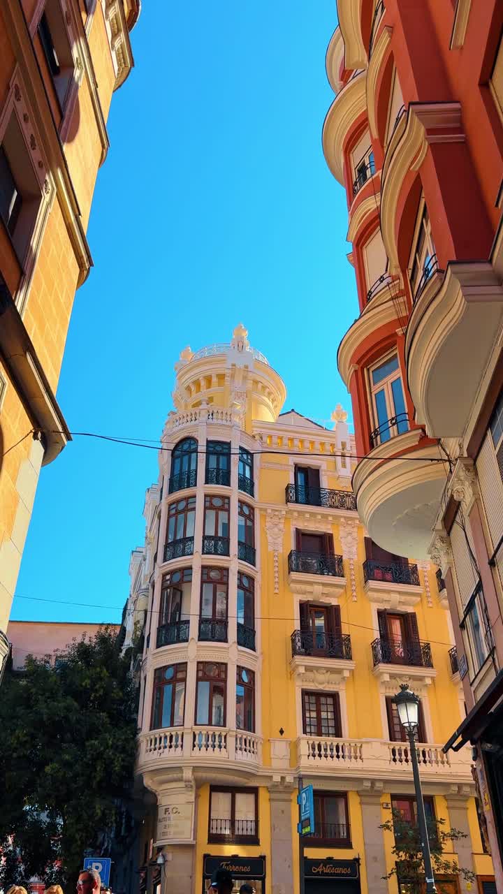 Alicante, Spanyol, 6 Agustus 2025: Arsitektur bersejarah berwarna kuning dan merah di pusat kota Alicante. Tampilan sudut rendah bangunan tradisional penuh warna dengan balkon berukir dengan latar belakang langit biru cerah