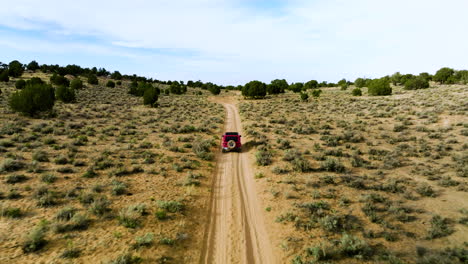 aerial follow red jeep wrangler driving on dirt road towards white pocket in utah, usa