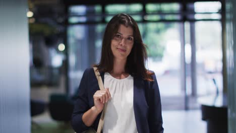 retrato de una mujer de negocios caucásica sonriente con cabello marrón caminando en una oficina moderna