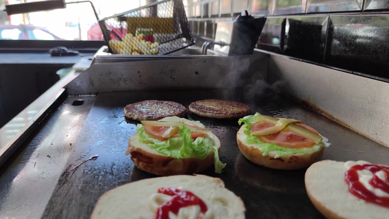 業務用の厨房でハンバーグパティを焼き、パンを準備するシェフ