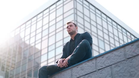 low-angle-shot-handsome-man-sits-on-parapet-against-building