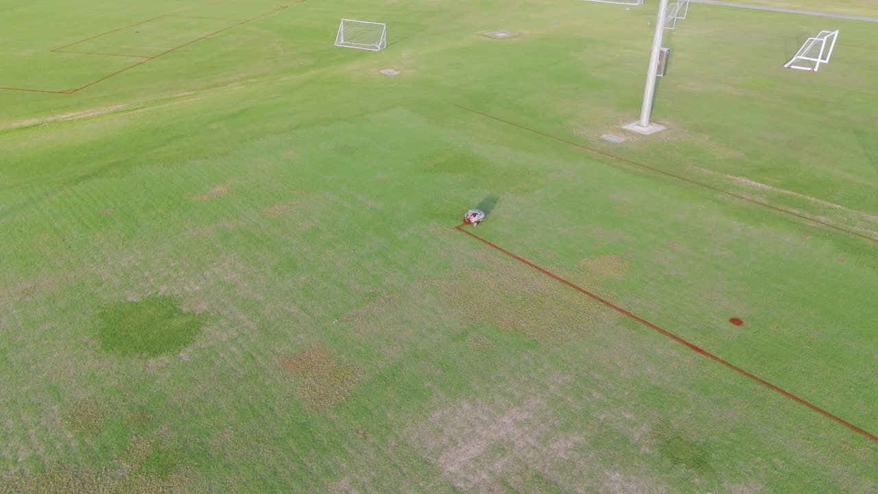 A remote-controlled robot paints precise lines on a soccer field under bright daylight