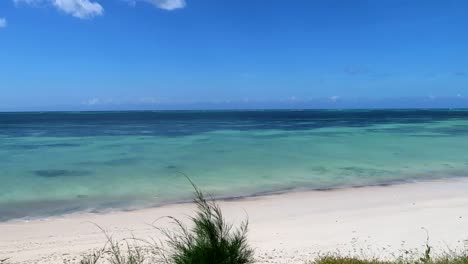 Panning-left-shot-revealing-an-empty-tropical-sunny-beach-with-turquoise-water-in-paradisiacal-landscape