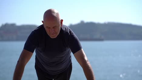 Concentrated-mature-man-doing-push-ups-at-riverside